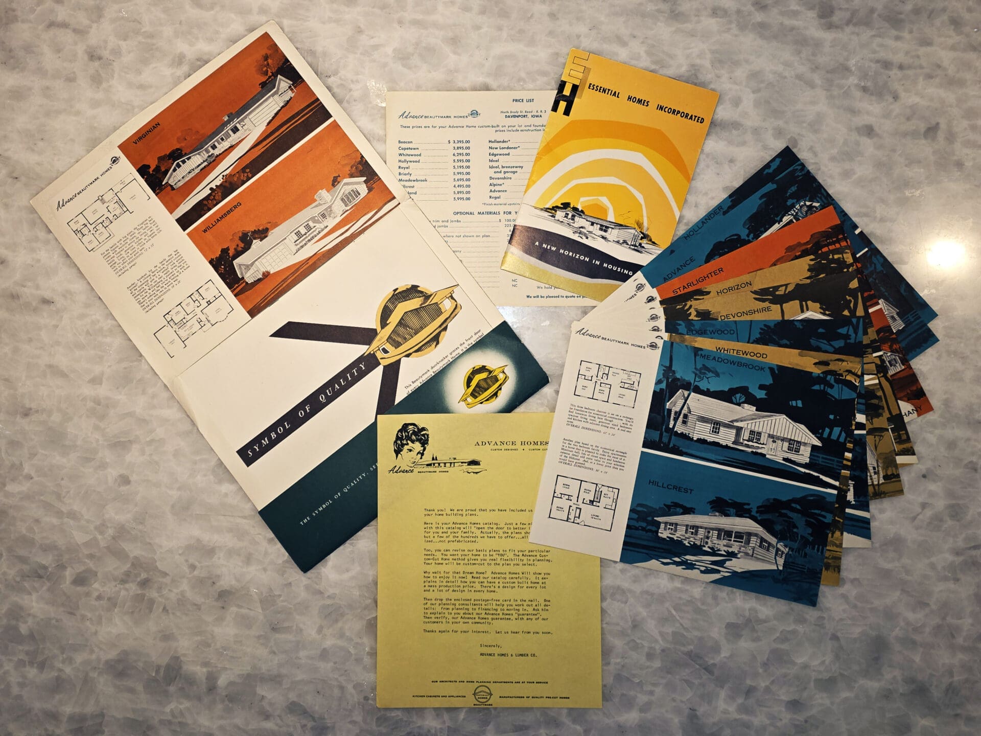 Vintage Advance Homes brochures and floorplan flyers fanned out on a marbled tabletop, showing mid-century house illustrations, model names, price list and company logo reflecting decades of single-family home building by the Seitz family and Advance Homes